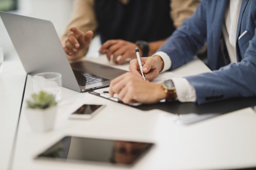 Close up of two people hands, signing documents with laptop on table in office image.